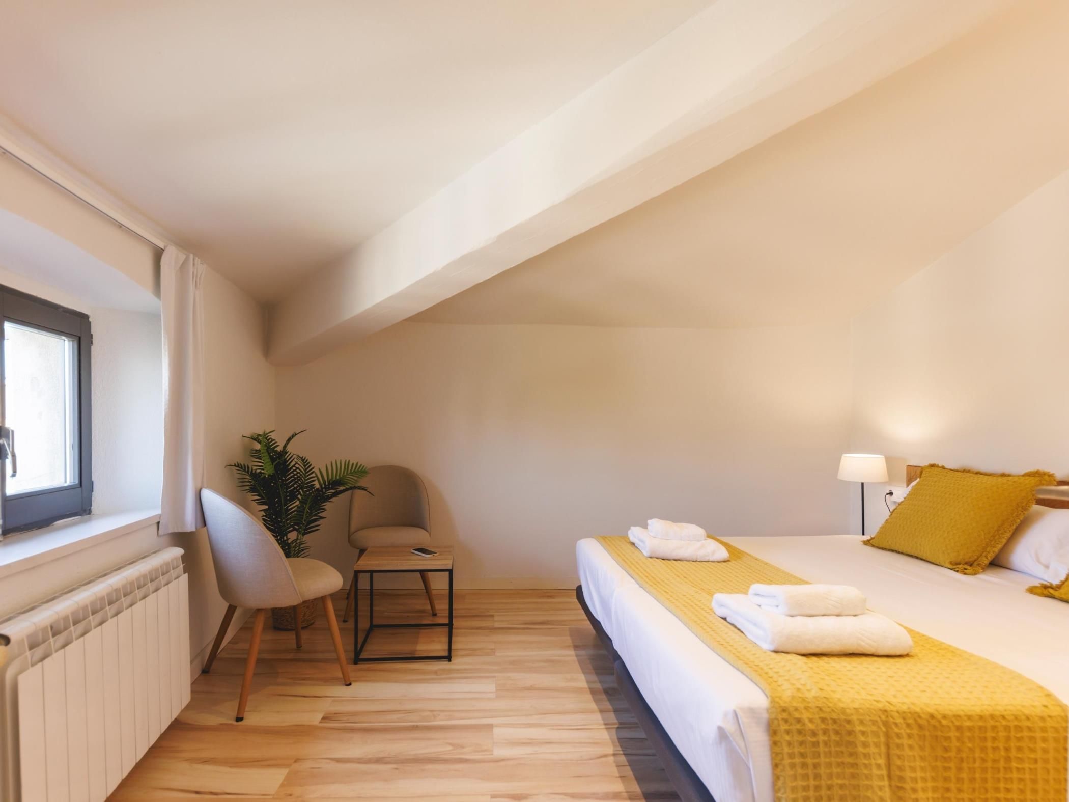 A hotel room with a bed, a desk, a chair, a radiator, and a window.