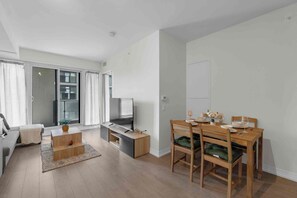 A modern living room with a sofa, coffee table, and a dining area with a wooden table and chairs. - City Center – Walkable 2BR, 5 min to Eaton Centre (Toronto)
