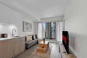 A modern living space with a kitchen, a sofa, a coffee table, and a TV. - City Center – Walkable 2BR, 5 min to Eaton Centre (Toronto)