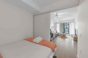 Ein modernes Schlafzimmer mit einem Bett, einem kleinen Tisch und Blick in den Wohnbereich.