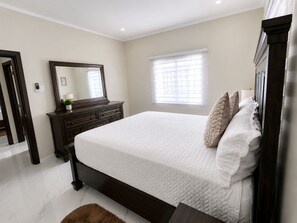 Une chambre à coucher avec un grand lit, une commode, un miroir et une fenêtre avec des stores.