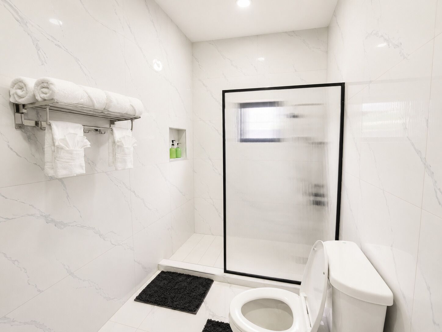 Et moderne badeværelse med en glasbrusekabine, toilet og en håndklæderække med pænt rullede håndklæder.