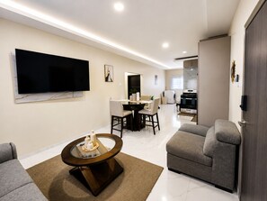Ein modernes Wohnzimmer mit Fernseher, rundem Couchtisch, zwei grauen Sofas und einem Essbereich mit Tisch und Stühlen.