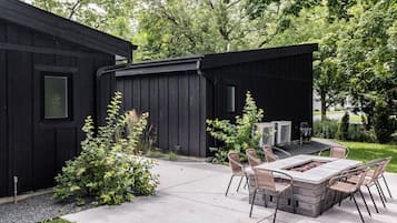 A black building with a patio area featuring a table and chairs, surrounded by greenery.