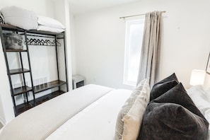 A hotel room with a bunk bed, a bedside table, a lamp, and a window with curtains.