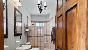 A bathroom with a wooden door, a chandelier, a toilet, a sink, and a mirror. - Beautiful Apartment with amazing views ! A hidden gem! (San José del Cabo)