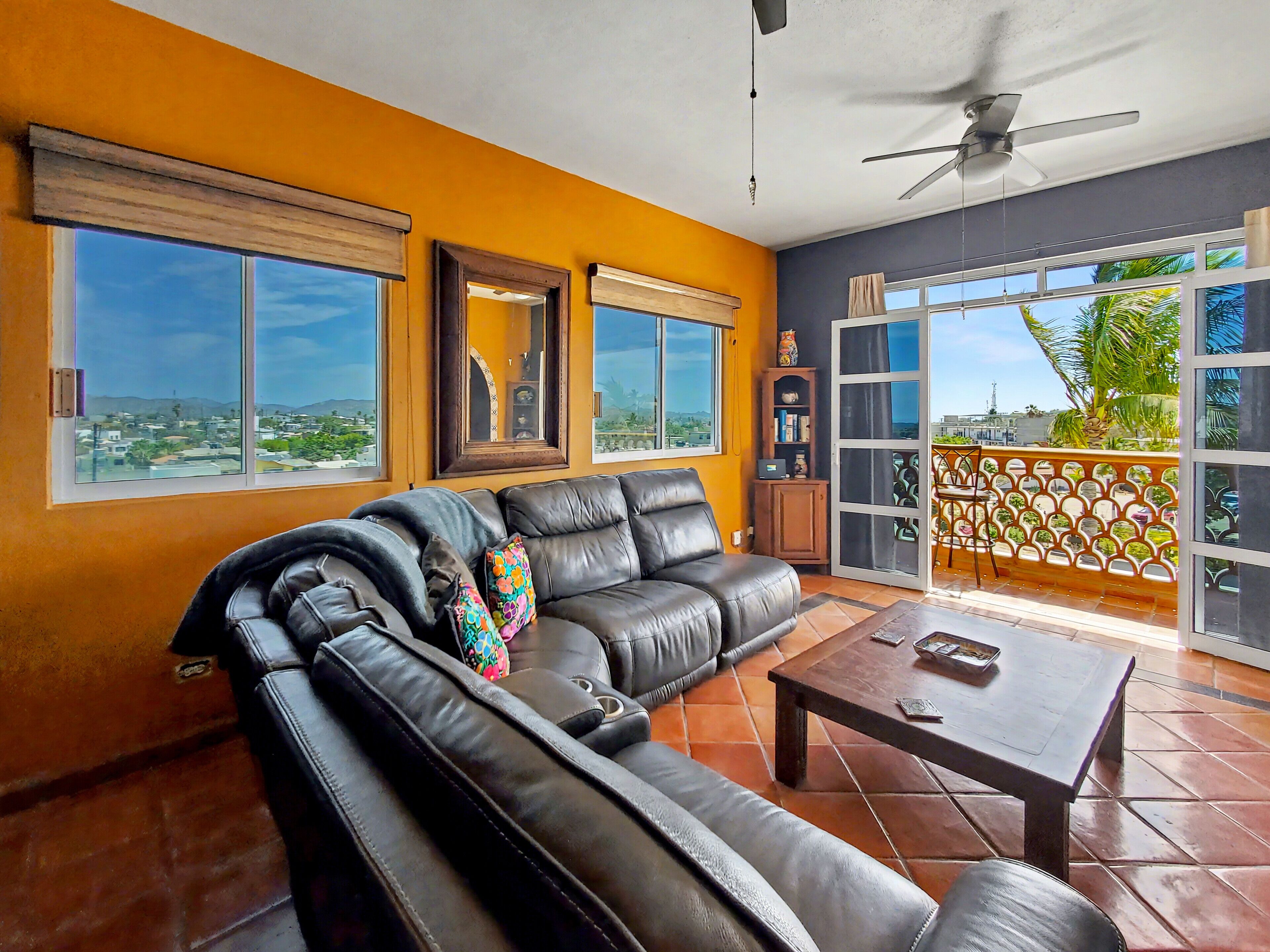 A living room with a black leather sofa, a coffee table, and a view of the city through large windows.