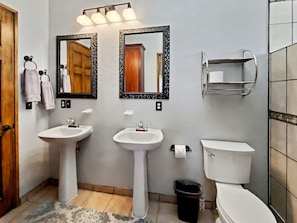 A bathroom with two sinks, a toilet, and two mirrors. There is a towel rack with towels, a trash bin, and a shelf with toiletries. - Beautiful Apartment with amazing views ! A hidden gem! (San José del Cabo)