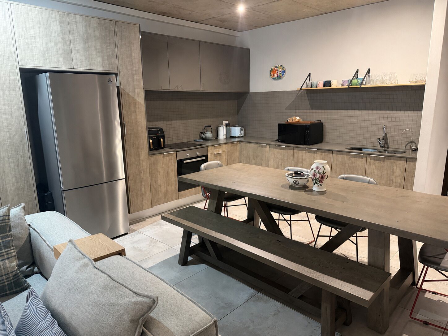 Une cuisine moderne équipée d’un réfrigérateur encastré, d’une table à manger avec des bancs et d’un four à micro-ondes.