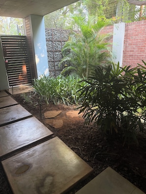 A garden area with a paved walkway, a stone wall, and various plants.