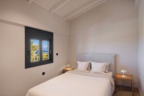 A bedroom with a bed, a nightstand, a lamp, and a window with a view of trees and a body of water.