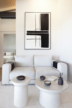 A modern living room with a white sofa, two white side tables, and a black abstract painting on the wall.
