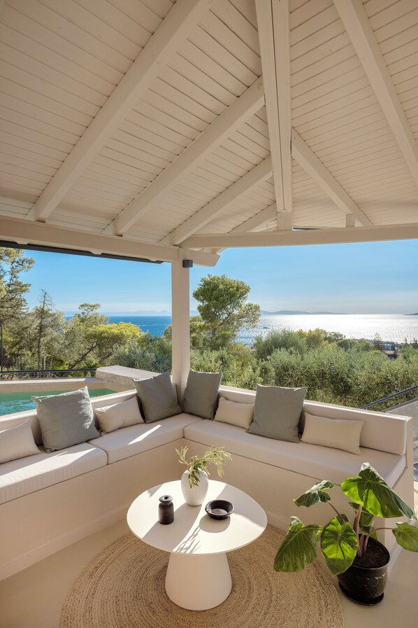 A covered outdoor seating area with a view of the sea and mountains.