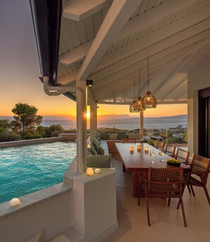 A terrace with a pool, dining area, and a view of the sea at sunset.