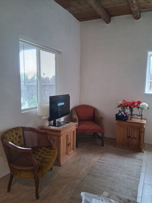 Ein Zimmer mit einem Fernseher auf einem Holztisch, einem roten Sessel, einem Holzschrank und einem Fenster mit Jalousien.