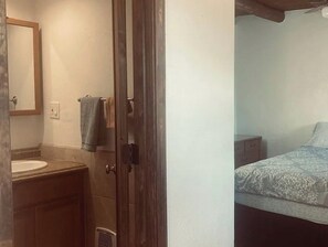 A bathroom with a sink, mirror, towel rack, and a door leading to a bedroom with a bed and nightstand. - Cozy Adobe-Style Santa Fe Condo Near Downtown (Santa Fe)