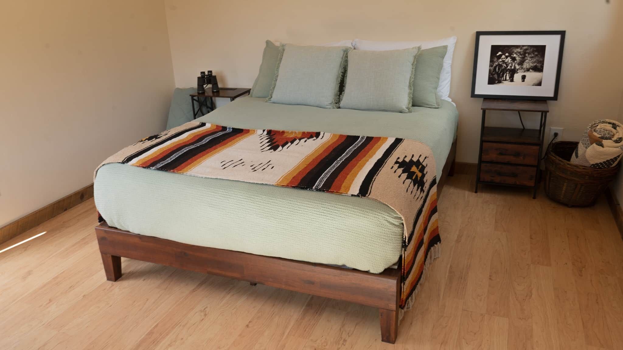 A bed with a striped blanket, a bedside table with a lamp, and a framed picture on the wall.