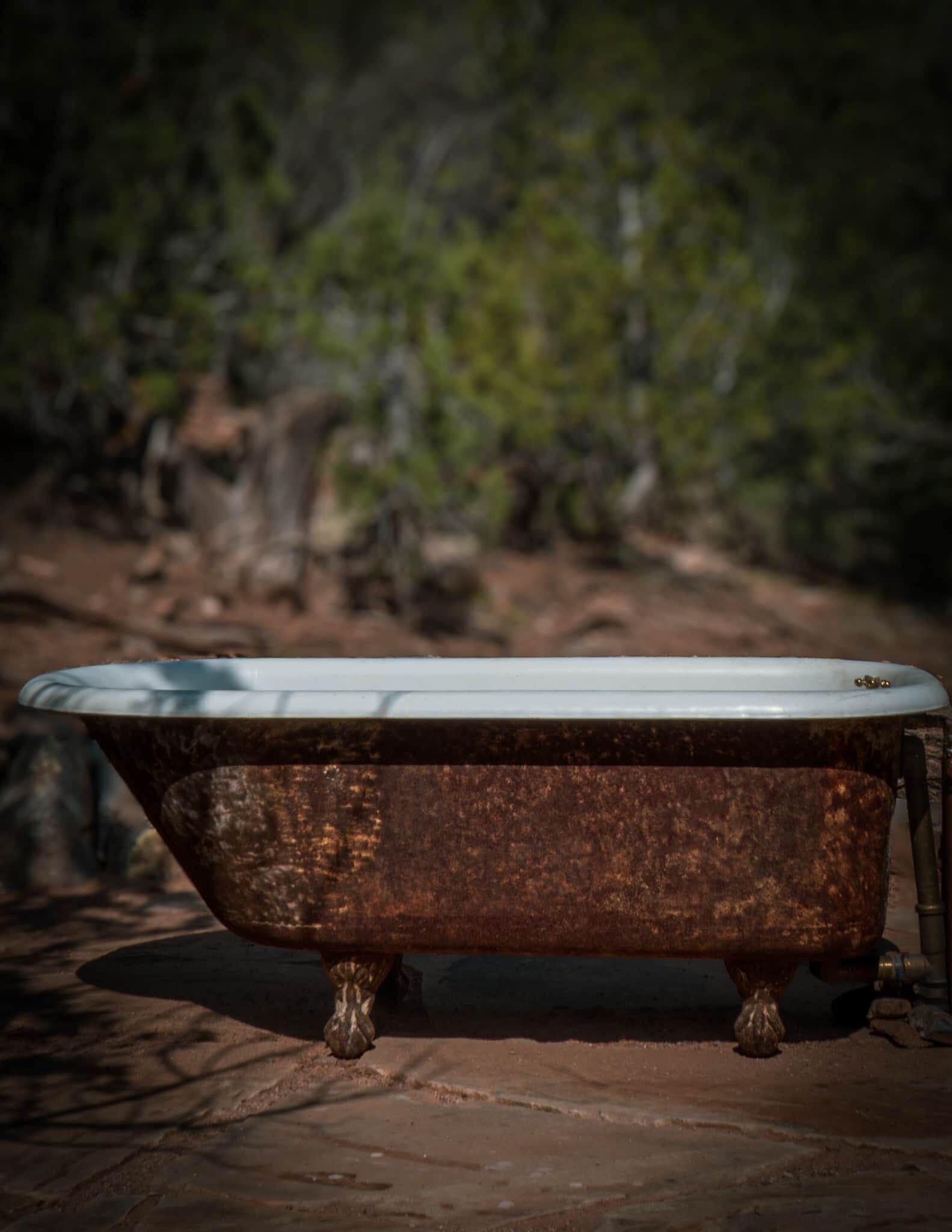 An old bathtub with a white interior, placed outdoors on a rocky surface.