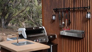 Et udendørs madlavningsområde med grill, vask og hængende køkkenredskaber.