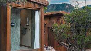 A modern cabin with a glass-enclosed shower area, wooden exterior, and a view of a mountainous landscape. - Outlaw Camp (Mesa County)