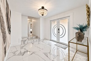 A modern interior with a marble floor, a chandelier, and a glass door with a circular design. - Belari Oasis - 5BR Miami Home, Heated Pool & Games (Miami)