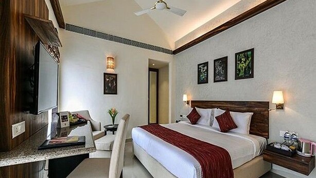 A hotel room with a bed, bedside table, desk, chair, and artwork on the wall. - Tropicana Resort and Spa Alibaug (Alibag)