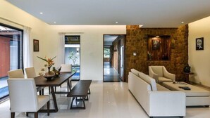 A modern living room with a dining area, a stone accent wall, and a view through a glass door. - Tropicana Resort and Spa Alibaug (Alibag)