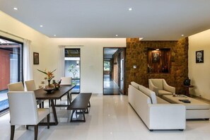 A modern living room with a dining area, a stone accent wall, and a view through a glass door. - Tropicana Resort and Spa Alibaug (Alibag)