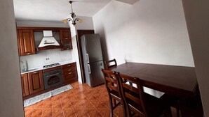 A compact kitchen with wooden cabinets, a stainless steel refrigerator, and a dining table with chairs. - Between the Sea and the Sky: Ponza - New Apartment (Ponza)