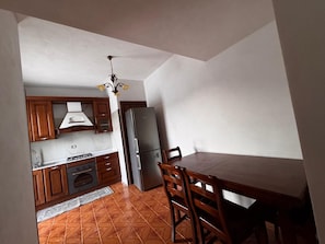Cozinha compacta com armários de madeira, geladeira de aço inoxidável e mesa de jantar com cadeiras.