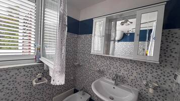 A bathroom with a bidet, a sink, a mirror, and a window with blinds.