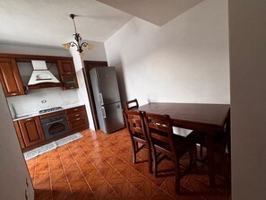A compact kitchen with a stove, oven, refrigerator, and wooden dining table with chairs. - Between the Sea and the Sky: Ponza - New Apartment (Ponza)