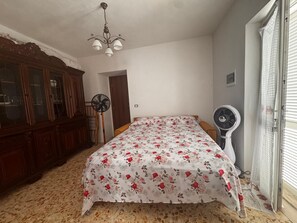 A bedroom with a bed, a wooden cabinet, a standing fan, and a ceiling fan. - Between the Sea and the Sky: Ponza - New Apartment (Ponza)