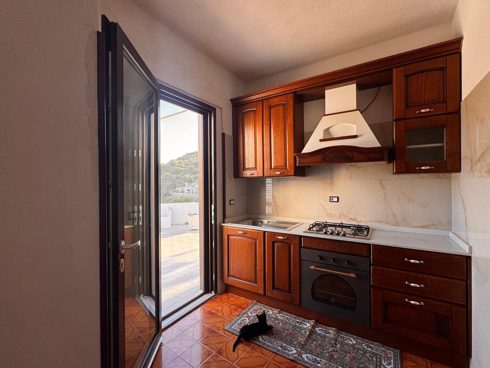 A kitchen with wooden cabinets, a gas stove, and a view through a sliding glass door.