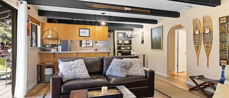 A modern living room with a leather sofa, a wooden coffee table, and a kitchen area in the background.