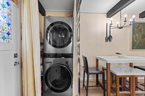 A compact laundry room with two front-loading washing machines, a dining area with a table and chairs, and a stained glass window. - Cortina Chalet - Cozy Lake Tahoe Retreat / Walk to Diamond Peak (Incline Village)