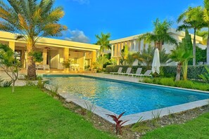 A swimming pool with lounge chairs and palm trees, surrounded by a well-maintained lawn and a building with columns. - The Hidden Pearl of Punta Cana in White Sands (Punta Cana)