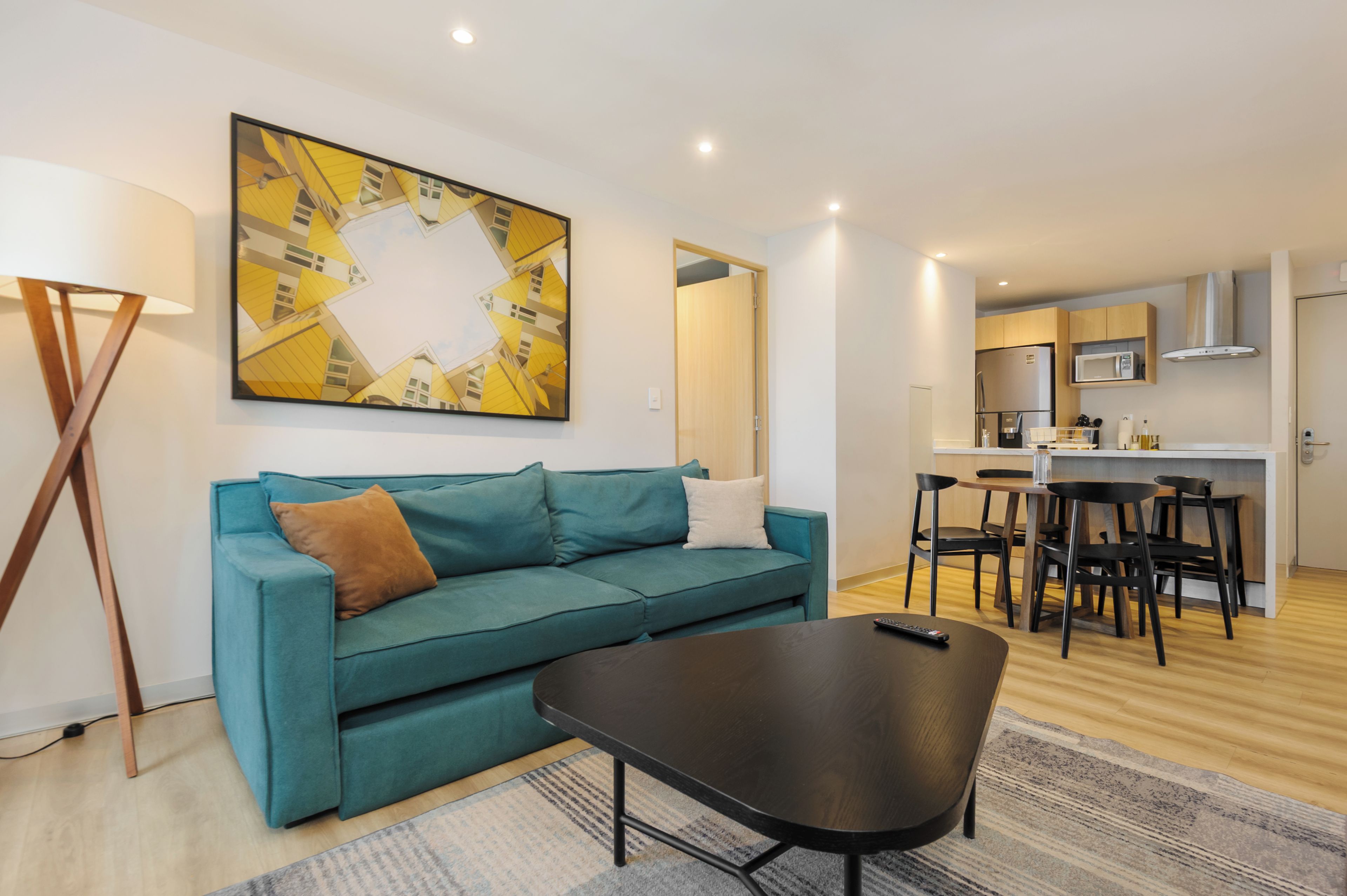 Una sala de estar moderna con un sofá color turquesa, una mesa de centro y un comedor con cocina al fondo.