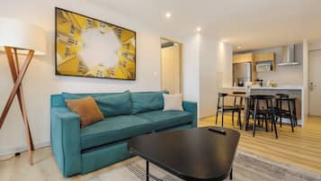 Una sala de estar moderna con un sofá color turquesa, una mesa de centro y un comedor con cocina al fondo.