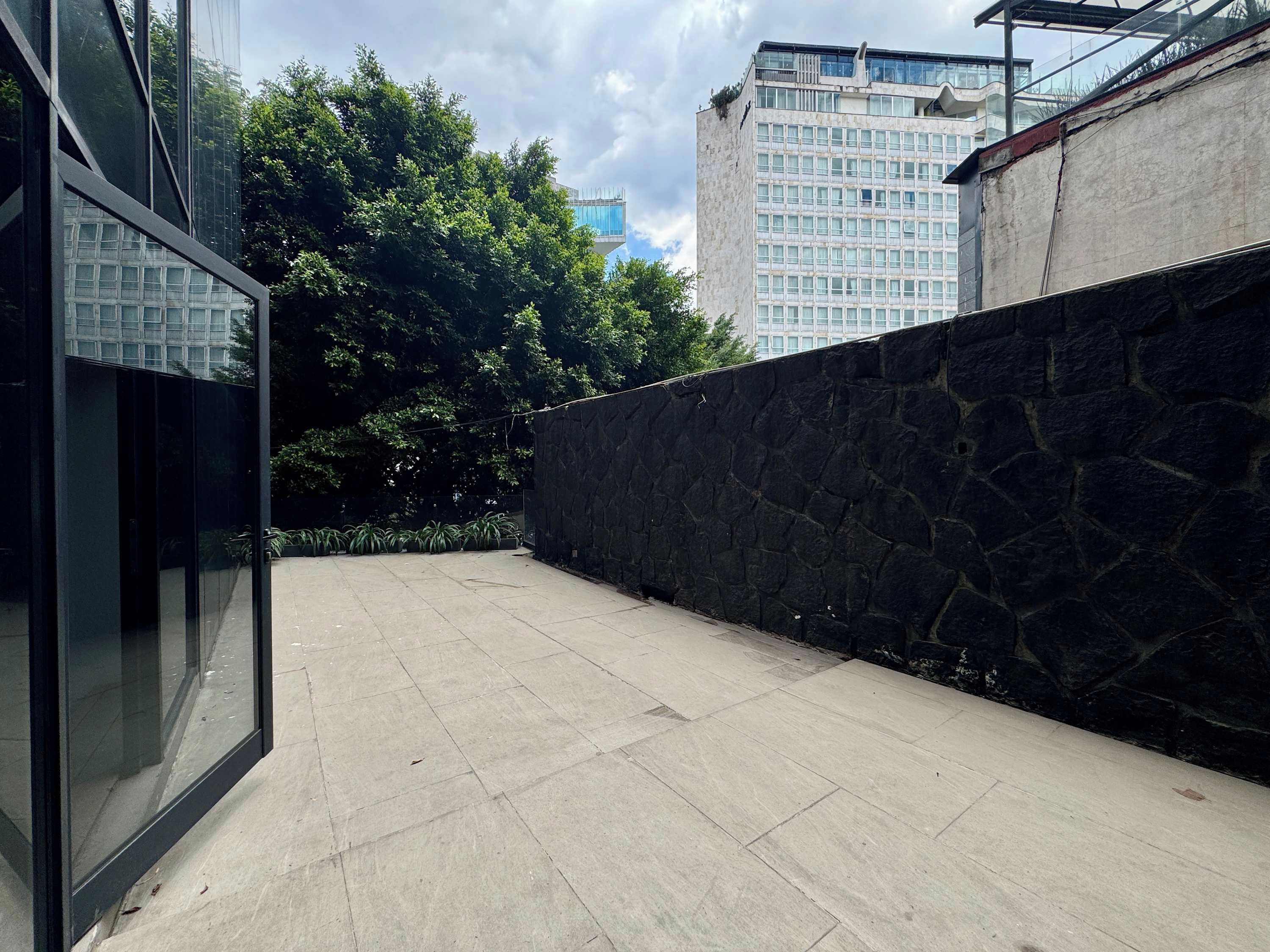 A courtyard with a stone wall, a glass building, and a view of a high-rise building.