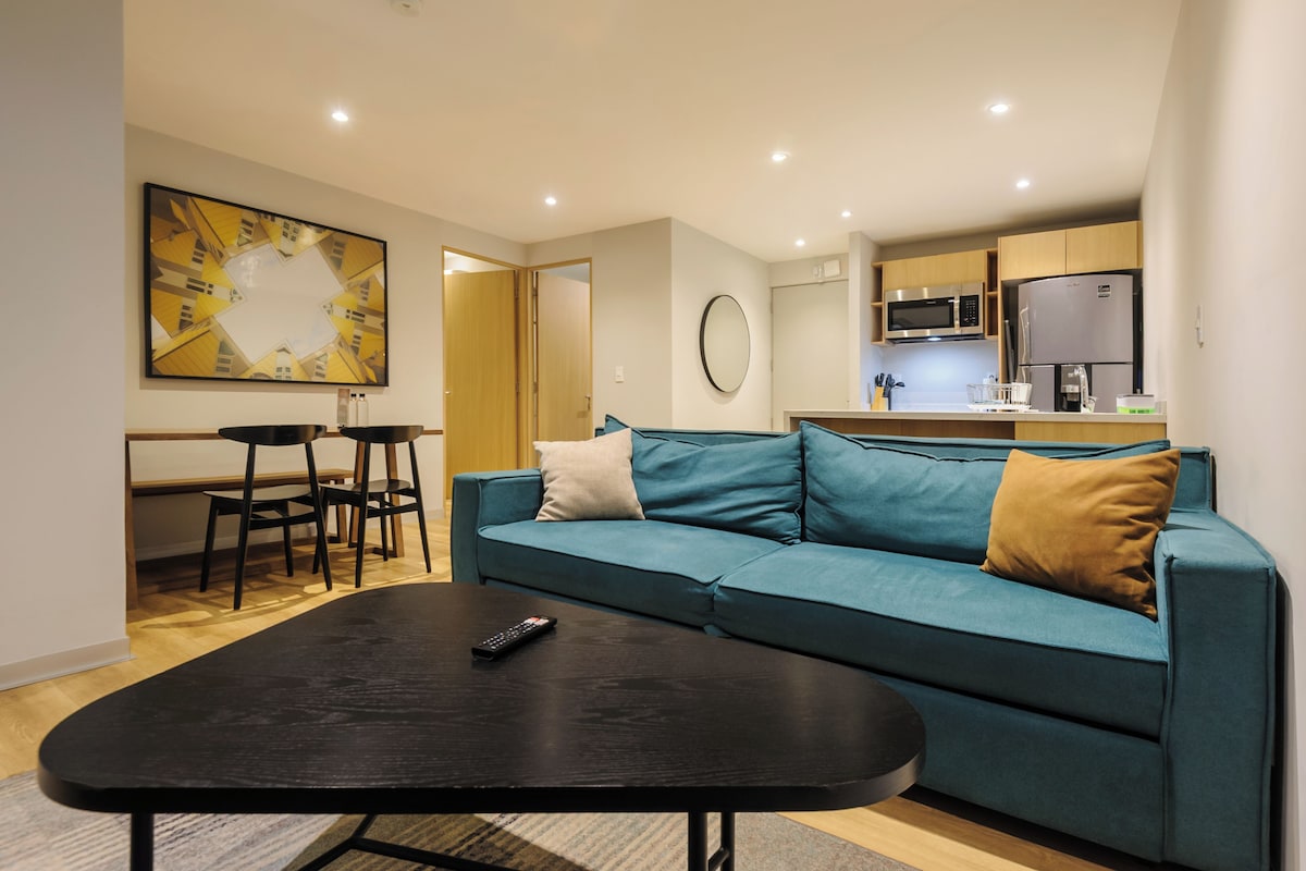 Uma sala de estar moderna com um sofá azul-esverdeado, uma mesa de centro preta e um espaço de jantar com mesa e cadeiras de madeira.