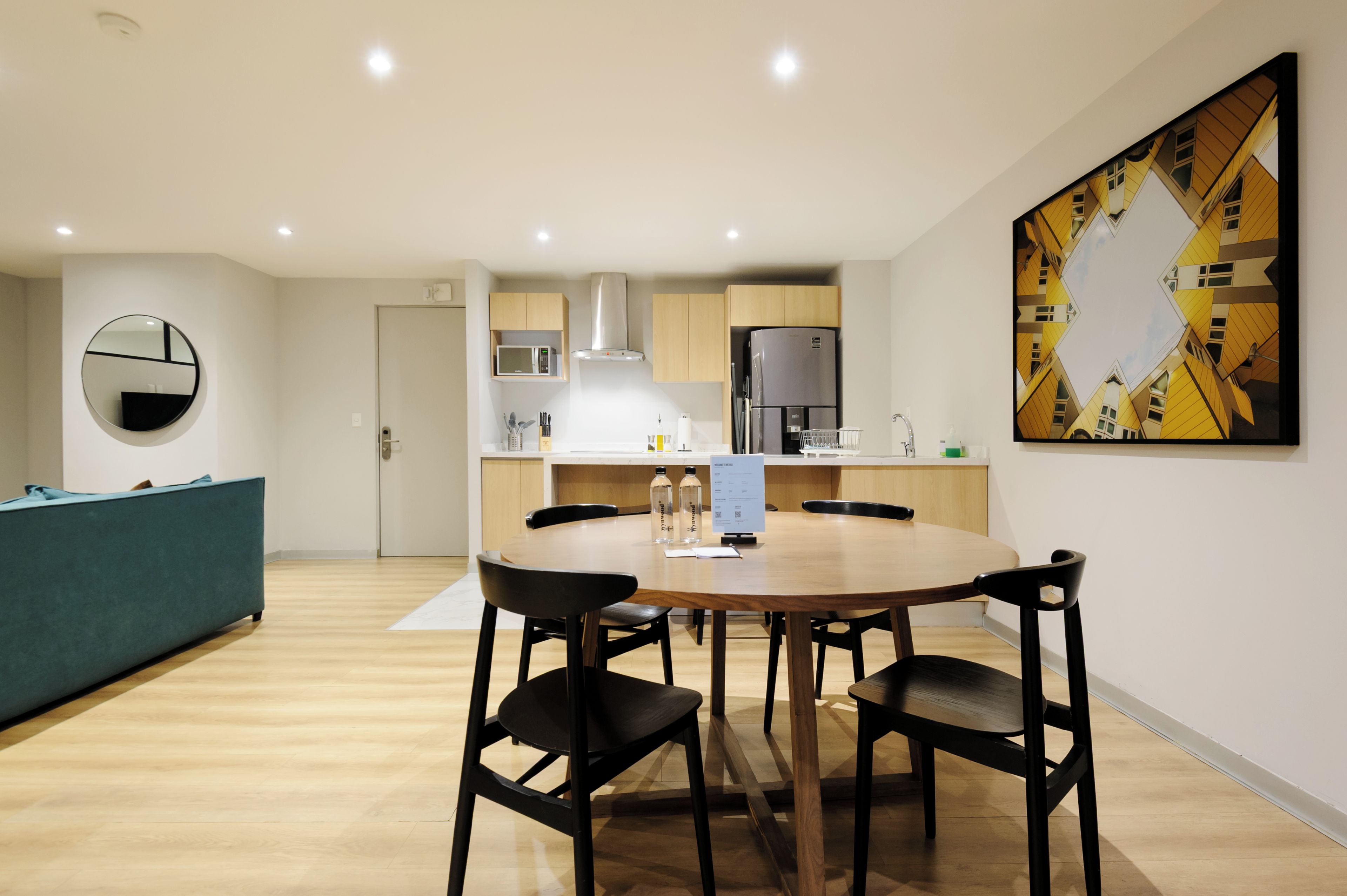 A modern kitchen with a dining area, a microwave, a refrigerator, and a large abstract painting on the wall.