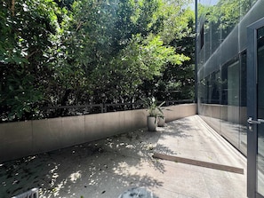 Um edifício moderno com fachada de vidro, um cachepot de concreto com planta em vaso e um espaço de pátio com ladrilhos.