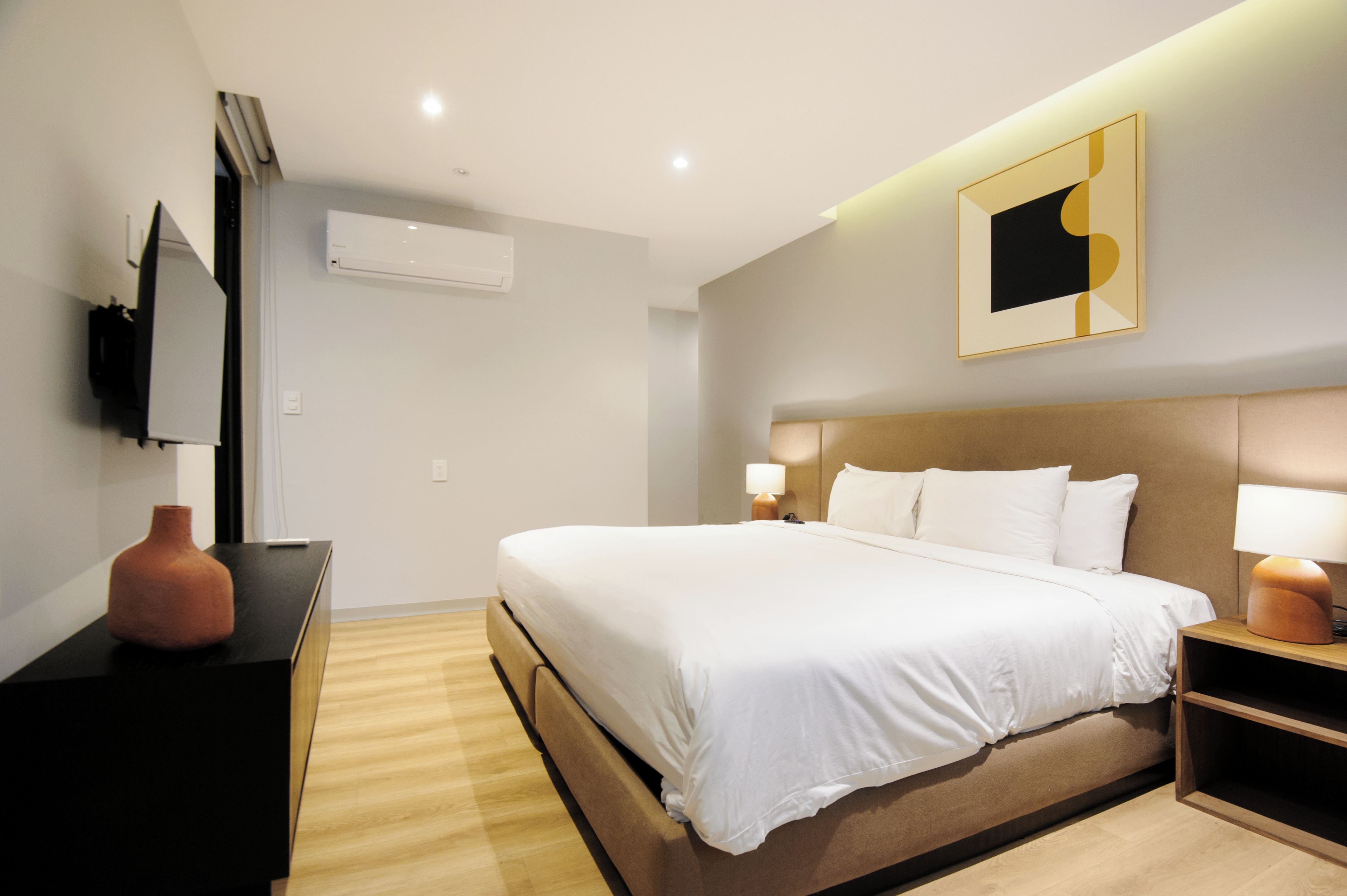 A hotel room with a bed, bedside lamps, a flat-screen TV, and a wall-mounted air conditioner.