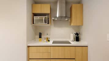 Uma cozinha compacta com armários de madeira, micro-ondas, exaustor de aço inoxidável e bancada com utensílios básicos.