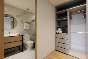 Um banheiro moderno com parede de mármore, pia com espelho, vaso sanitário e closet espaçoso com prateleiras e roupas penduradas.