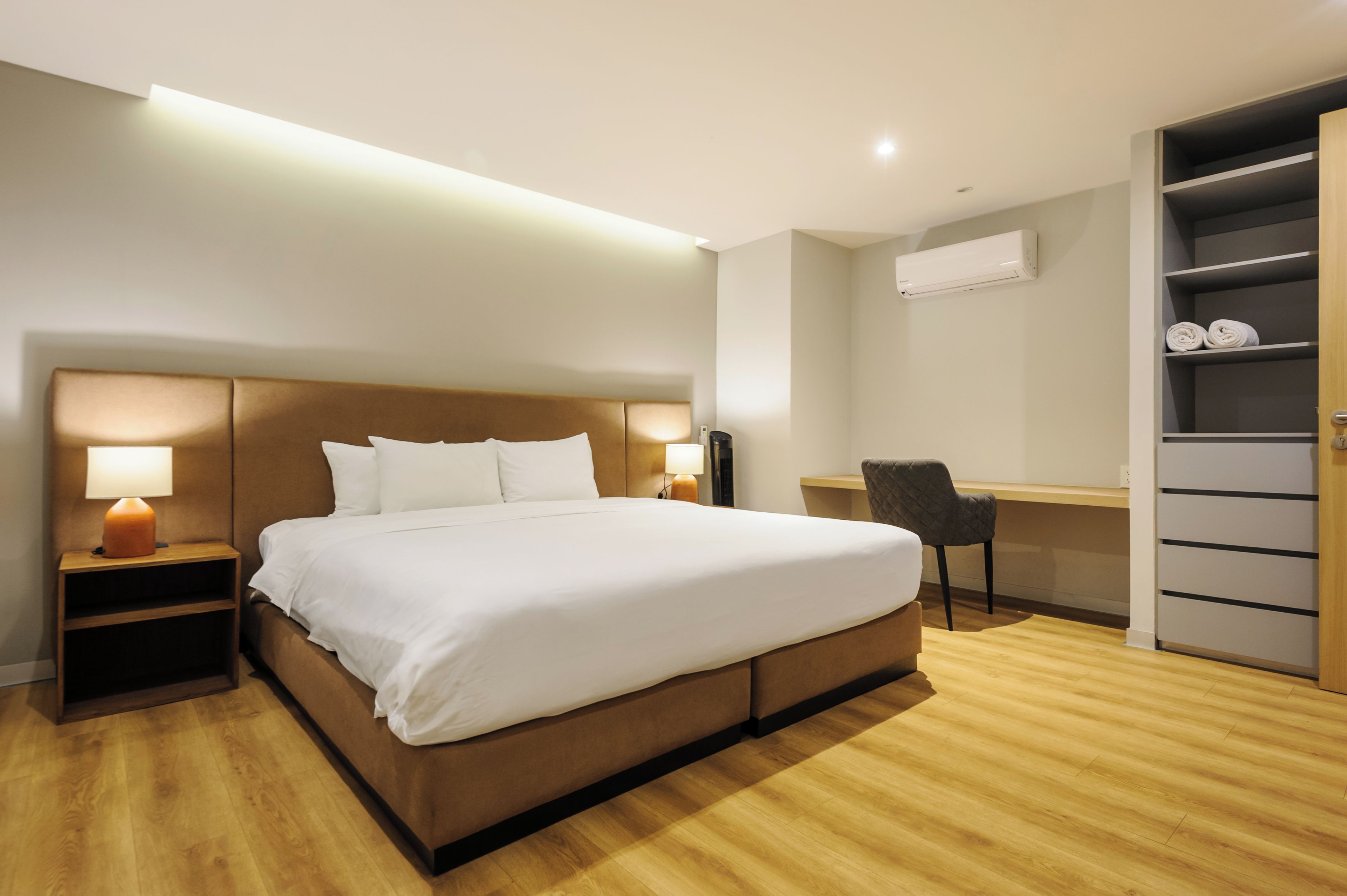 Ein Hotelzimmer mit einem großen Bett, Nachttischlampen, einem Schreibtisch, einem Stuhl, einem Kleiderschrank und einer Klimaanlage.