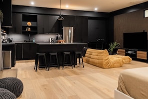 A modern kitchen with a central island, bar stools, a sofa, and a television.