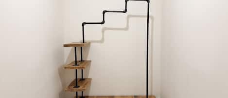 Un rincón con piso de madera y una escalera metálica de peldaños con repisas.