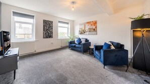 A modern living room with two sofas, a coffee table, a TV, and a floor lamp. - 5-Bed Flats Sleeping 11 · Free Parking · Near Beaumont Park, Huddersfield (Newsome)
